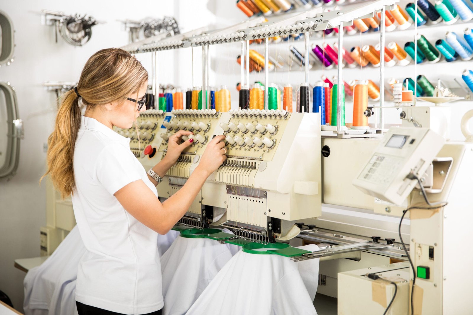 Young female worker preparing threads and garments on an embroidery machine